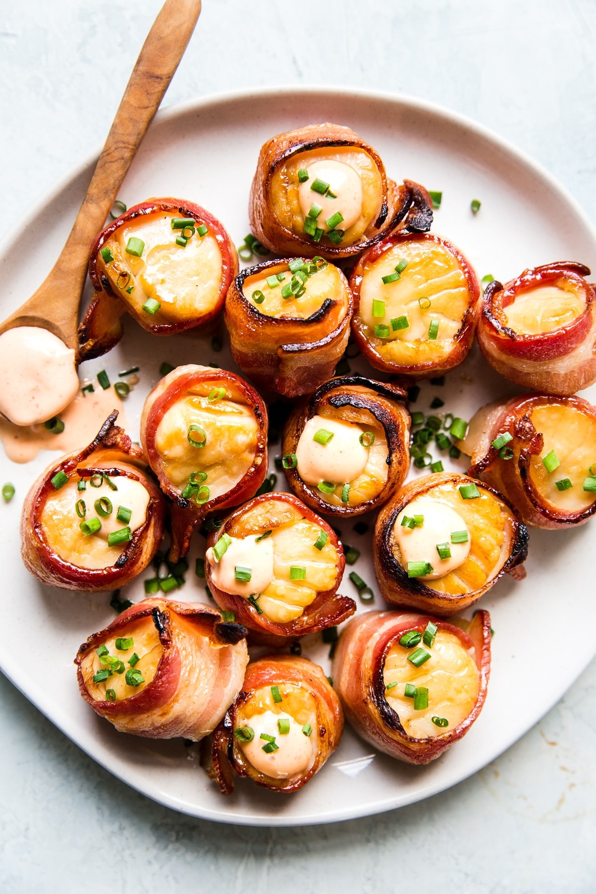 bacon wrapped sea scallops on a white plate with sriracha aioli and topped with fresh chives