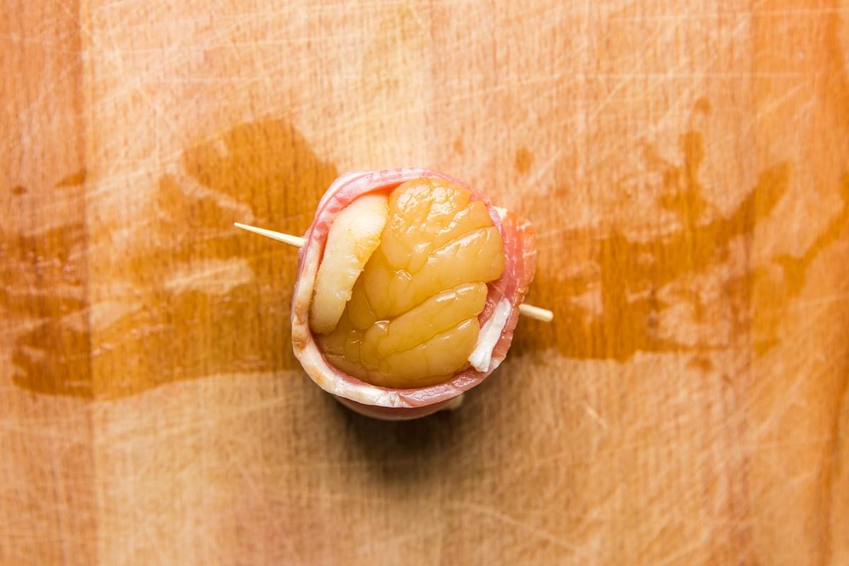 raw bacon wrapped sea scallop on a cutting board with a toothpick holding it together
