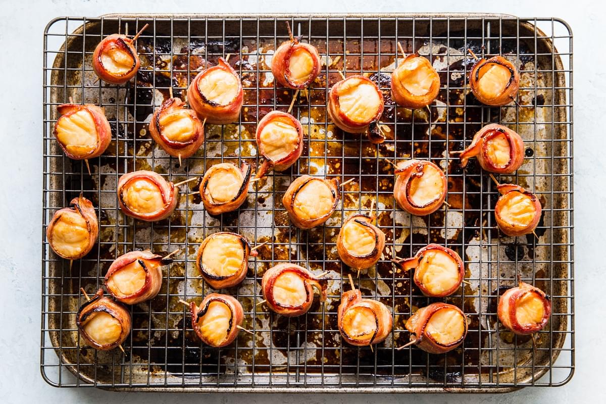 cooked bacon wrapped scallops on a cooling rack over a baking sheet