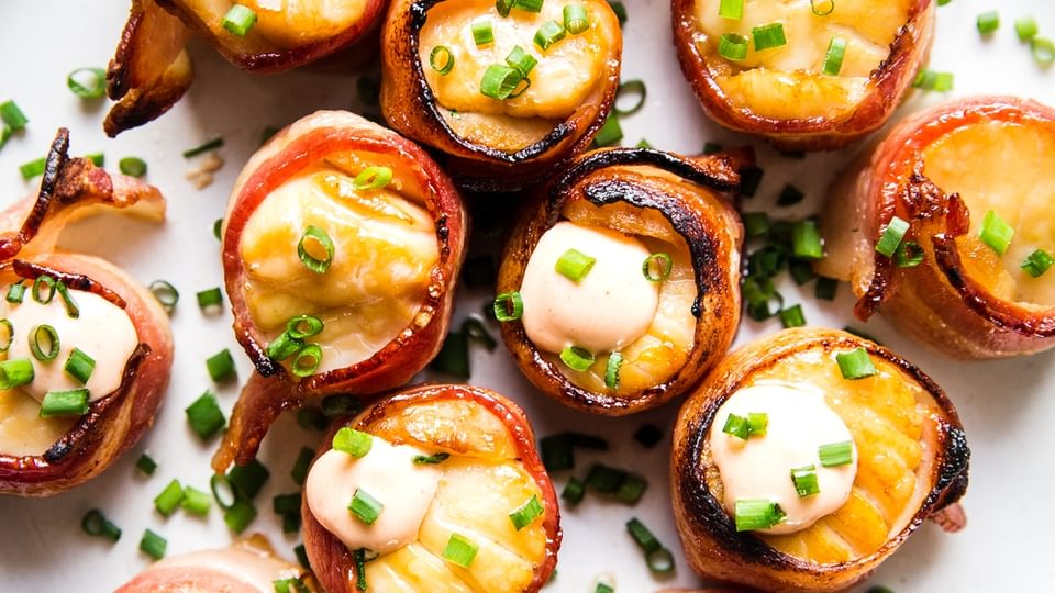 bacon wrapped sea scallops on a plate topped with fresh chives