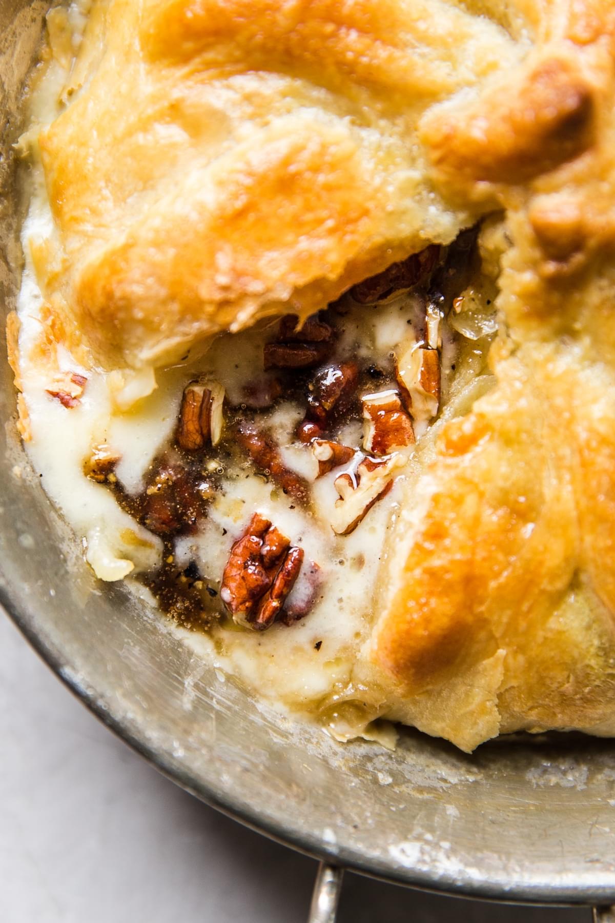 baked brie wrapped in puff pastry cut open with brie, pecans and brown sugar oozing out the center