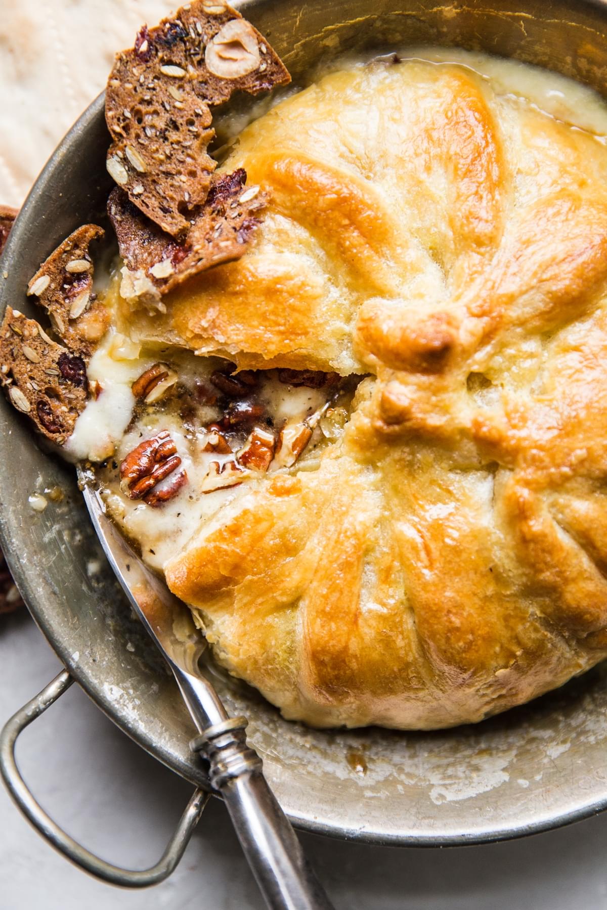 baked brie made with pecans, brown sugar and pepper wrapped in puffed pastry dough in baking dish being served with crackers