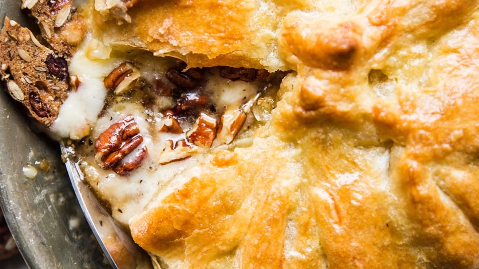 baked brie in a baking dish with pecans, brown sugar and crackers