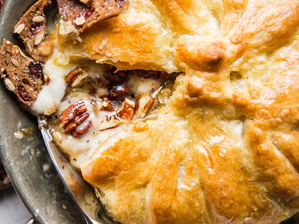 baked brie in a baking dish with pecans, brown sugar and crackers