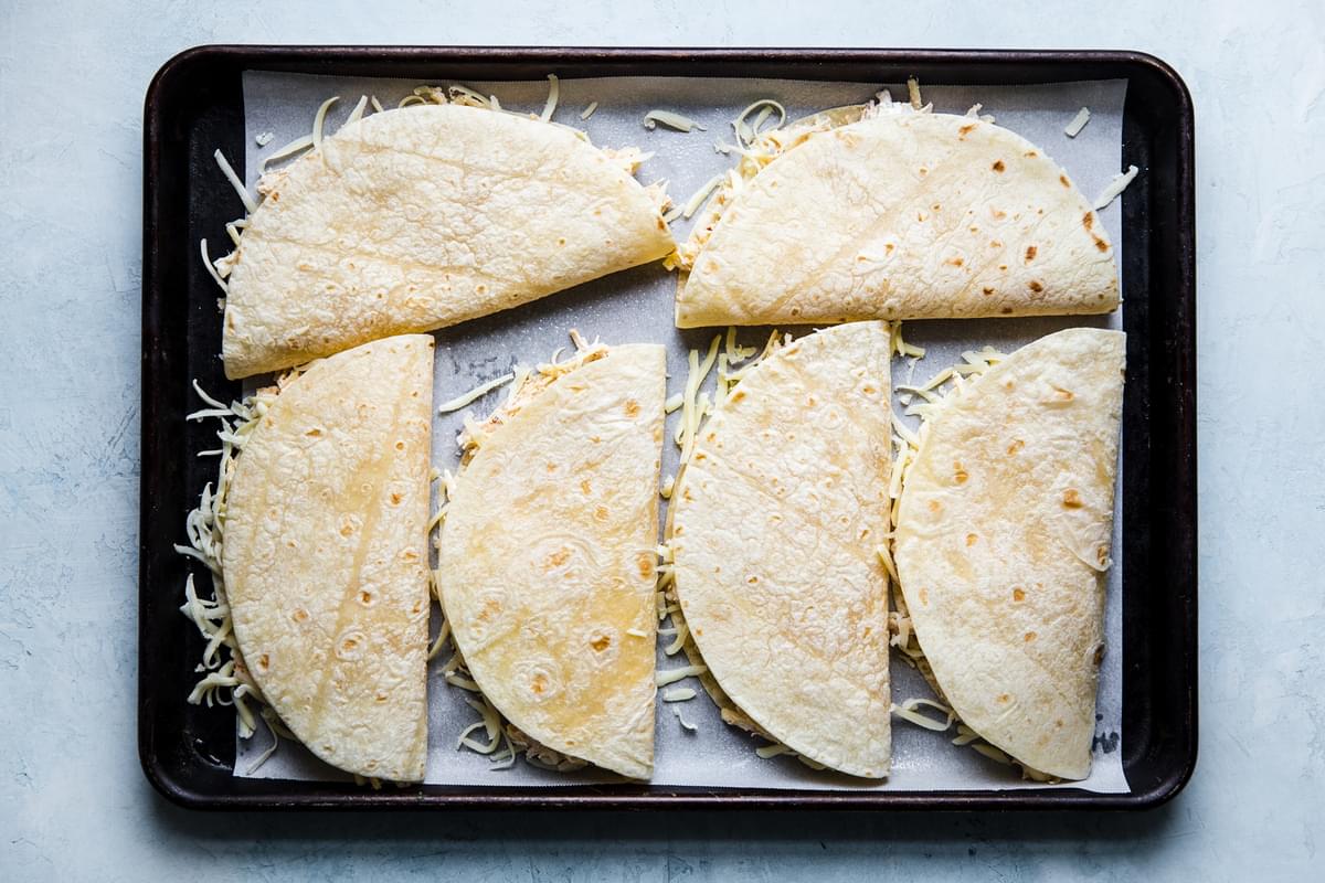 baking sheet lined with stuffed chicken quesadillas ready to be baked