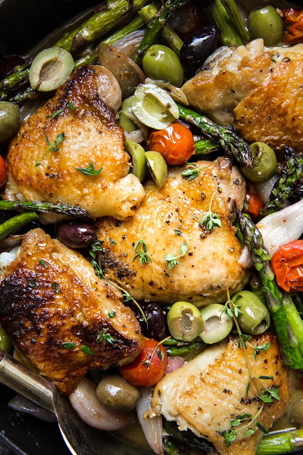 Baked Chicken Thighs With Asparagus close up in a pan with olives and tomatoes.