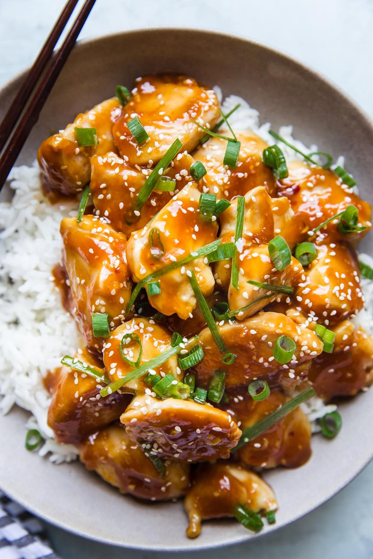 a bowl of homemade baked orange chicken on white rice topped with sesame seeds and green onions