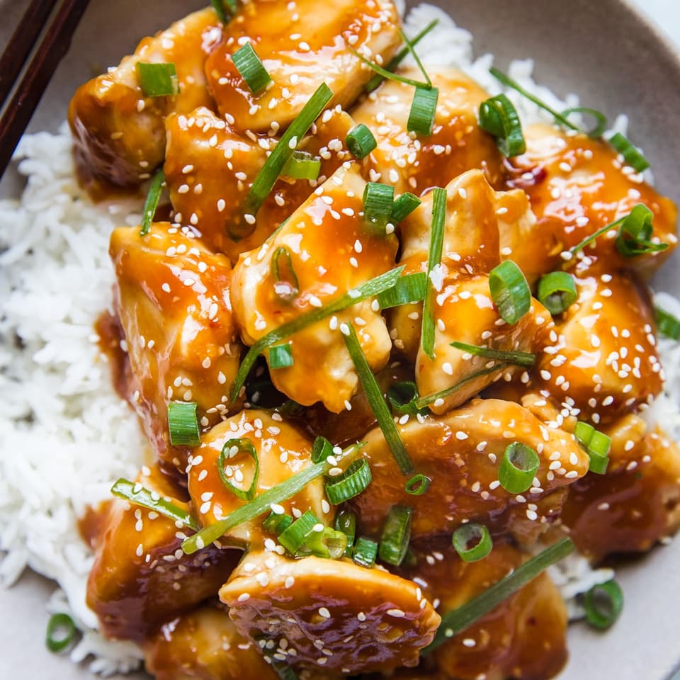 baked orange chicken on white rice topped with sesame seeds and green onions