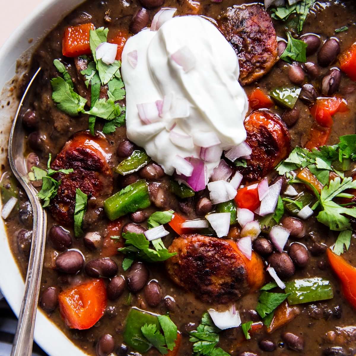a bowl of Black Bean Soup With Smoked Sausage and bell peppers topped with sour cream and cilantro