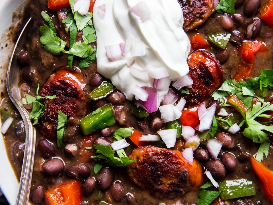 a bowl of Black Bean Soup With Smoked Sausage and bell peppers topped with sour cream and cilantro