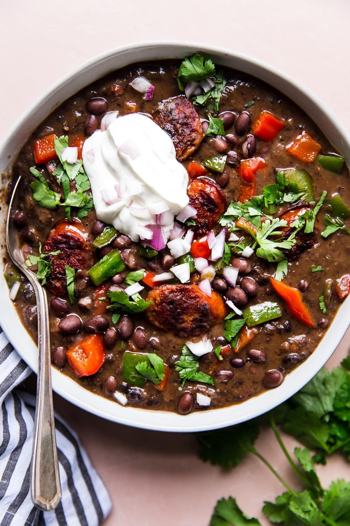 a bowl of homemade black bean soup with peppers, onions, and smoked sausage topped with sour cream and chopped cilantro