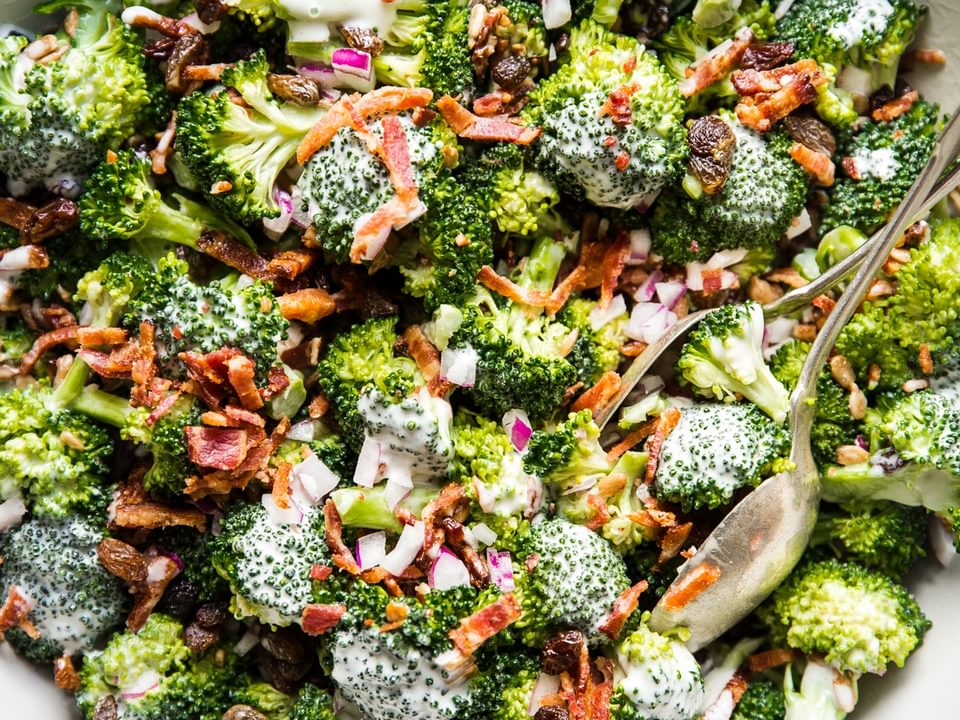 close up of homemade broccoli salad with creamy sweet dressing, crispy bacon, golden raisins and purple onions