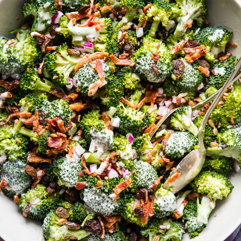 close up of homemade broccoli salad with creamy sweet dressing, crispy bacon, golden raisins and purple onions