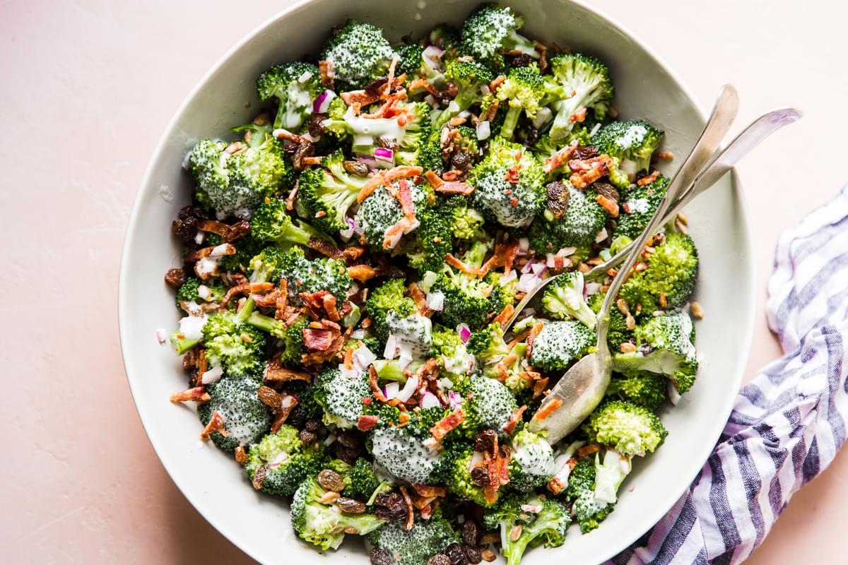 close up of homemade broccoli salad in a large bowl with salad tongs and a linen