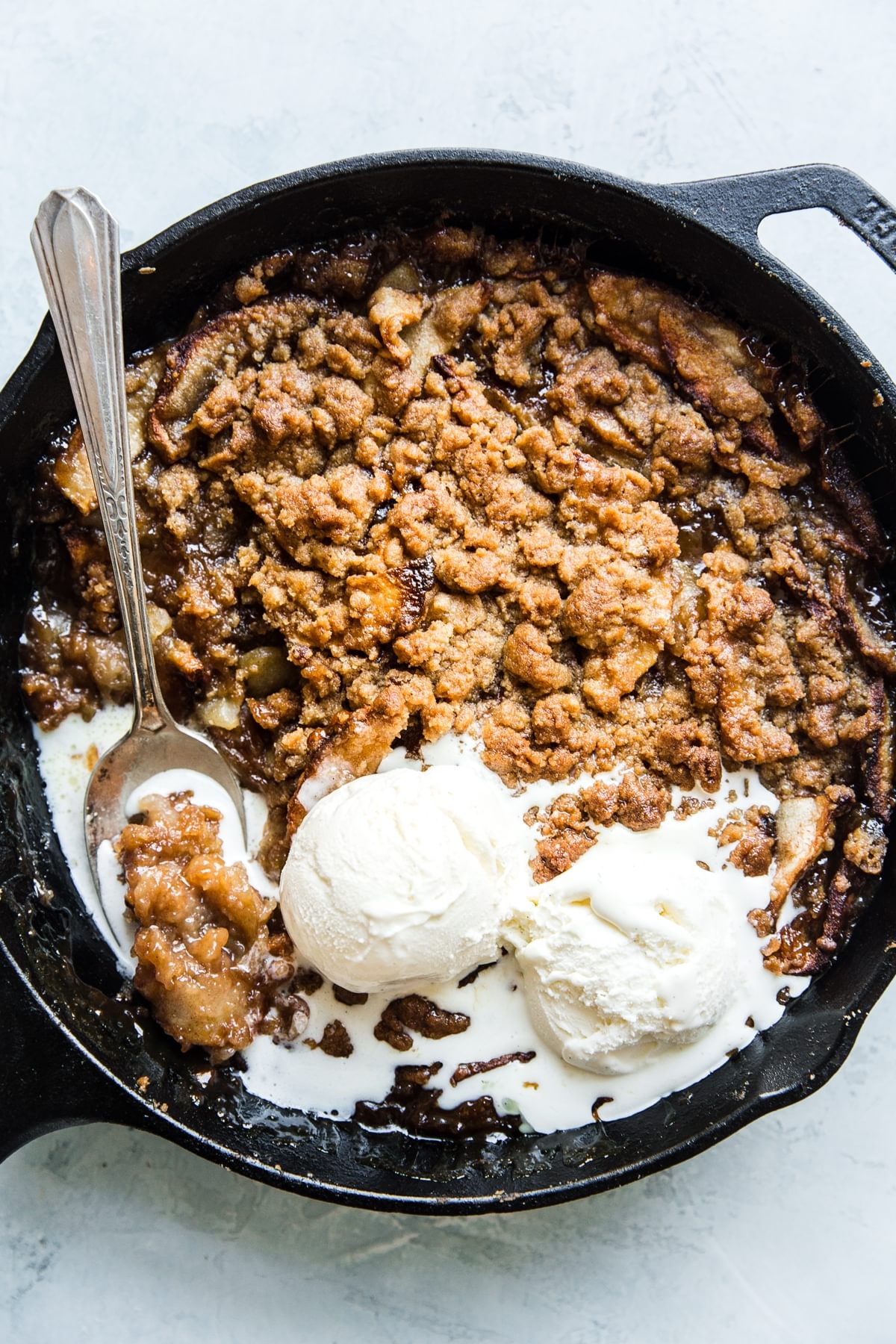 caramel apple crips in a black skillet topped with vanilla ice cream