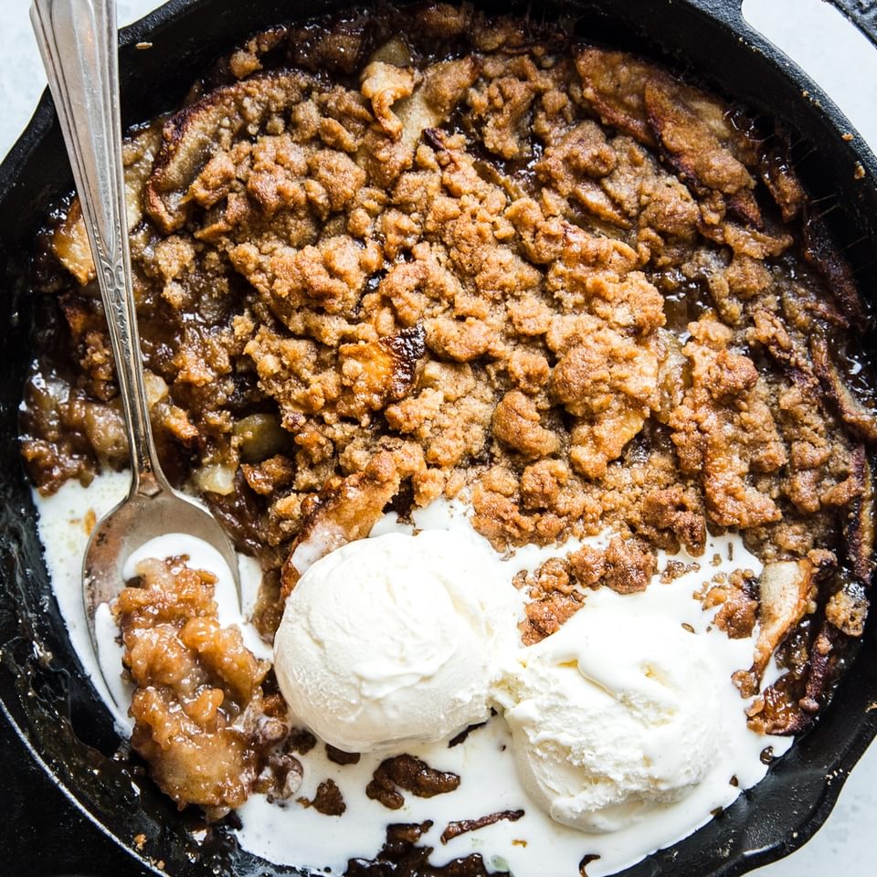 caramel apple crips in a black skillet topped with vanilla ice cream