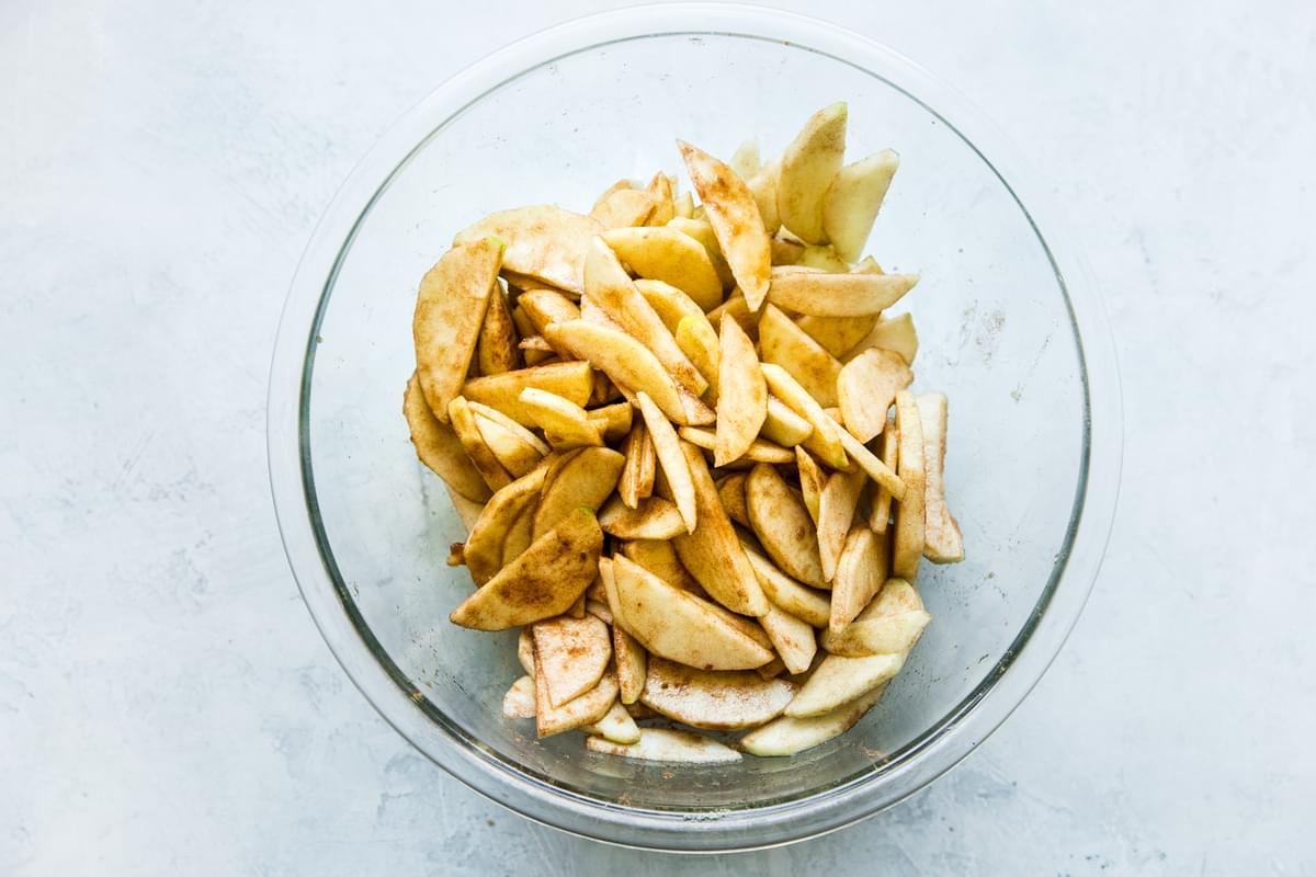 apple slices tossed with cinnamon and sugar in a glass bowl