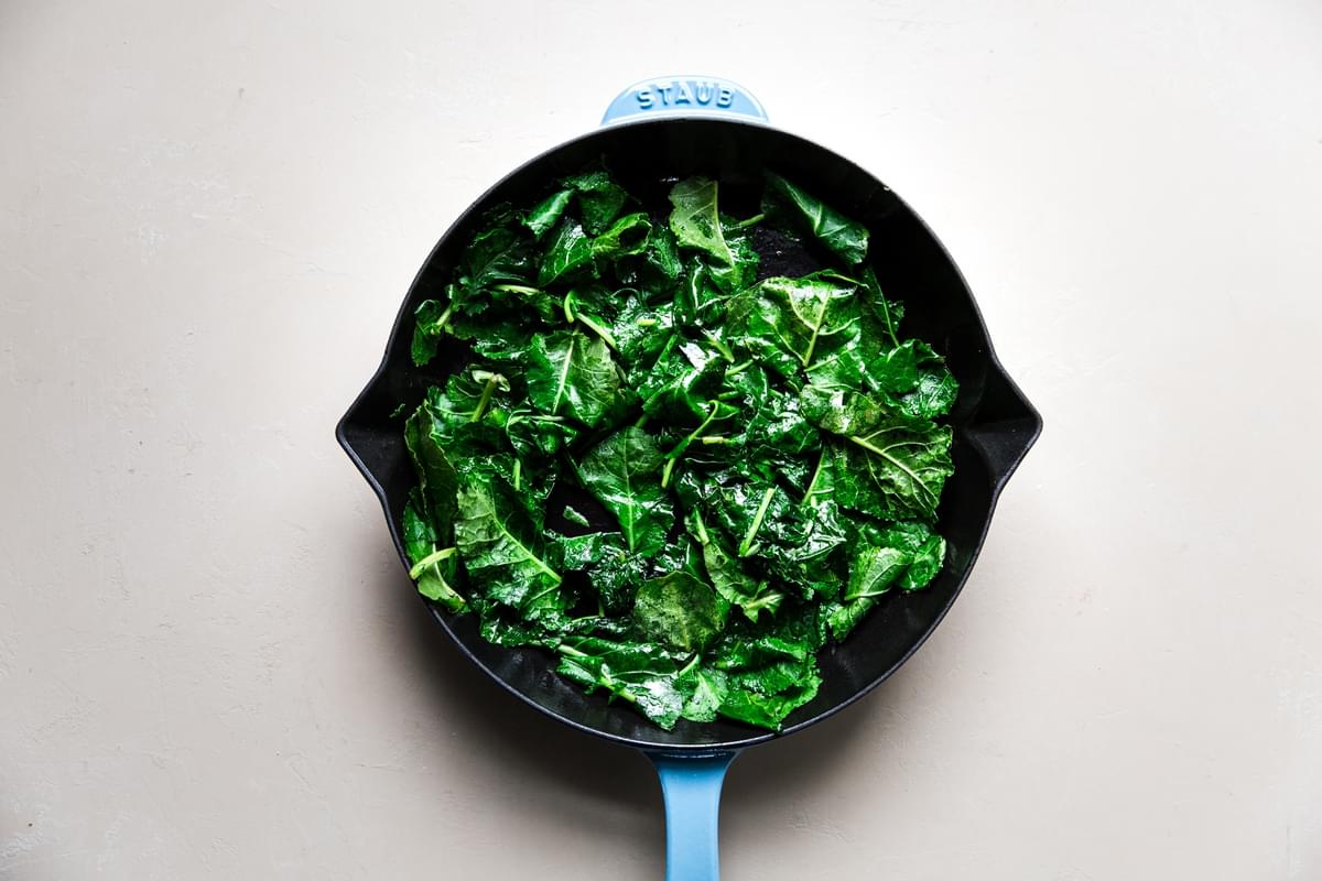 blue cast iron skillet with sautéed baby kale