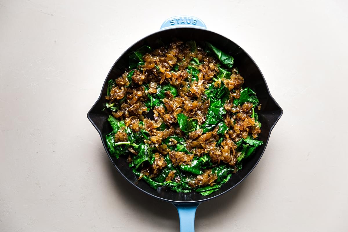 blue cast iron skillet with sautéed baby kale and caramelized onions