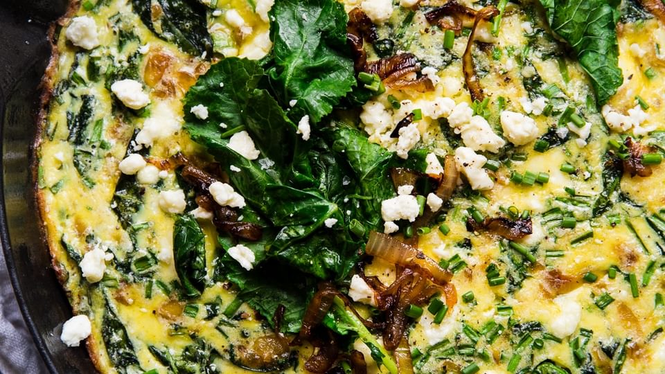 caramelized onion frittata in a blue cast iron skillet topped with baby kale, feta and caramelized onions