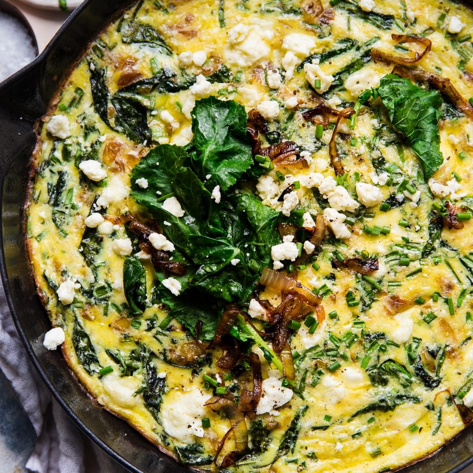 caramelized onion frittata in a blue cast iron skillet topped with baby kale, feta and caramelized onions