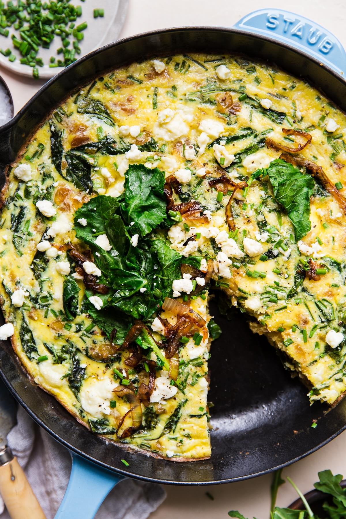 caramelized onion frittata in a blue cast iron skillet with one slice removed