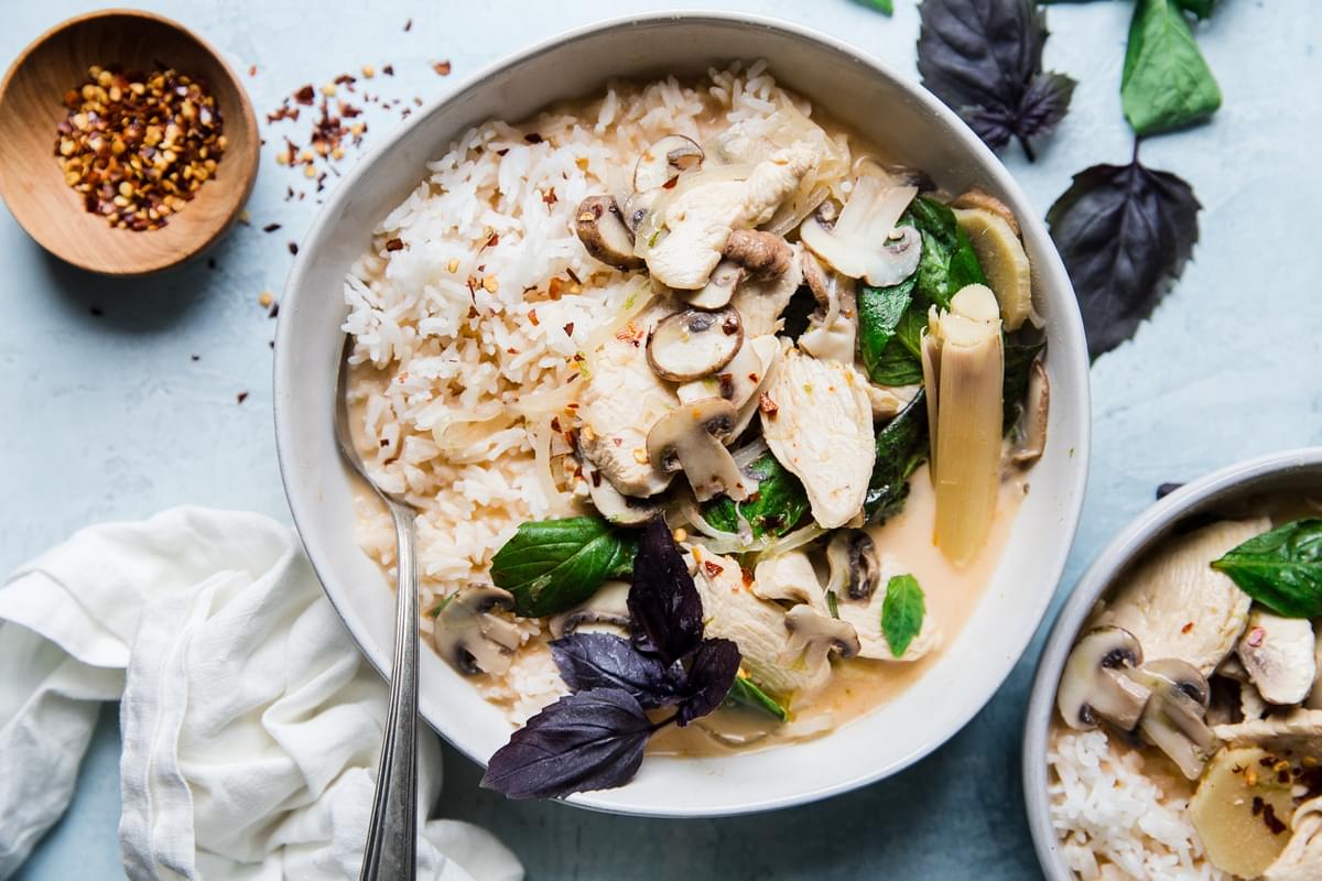 Coconut Chicken Soup Tom Kha Gai in a bowl with thai basil lemongrass, rice and a spoon