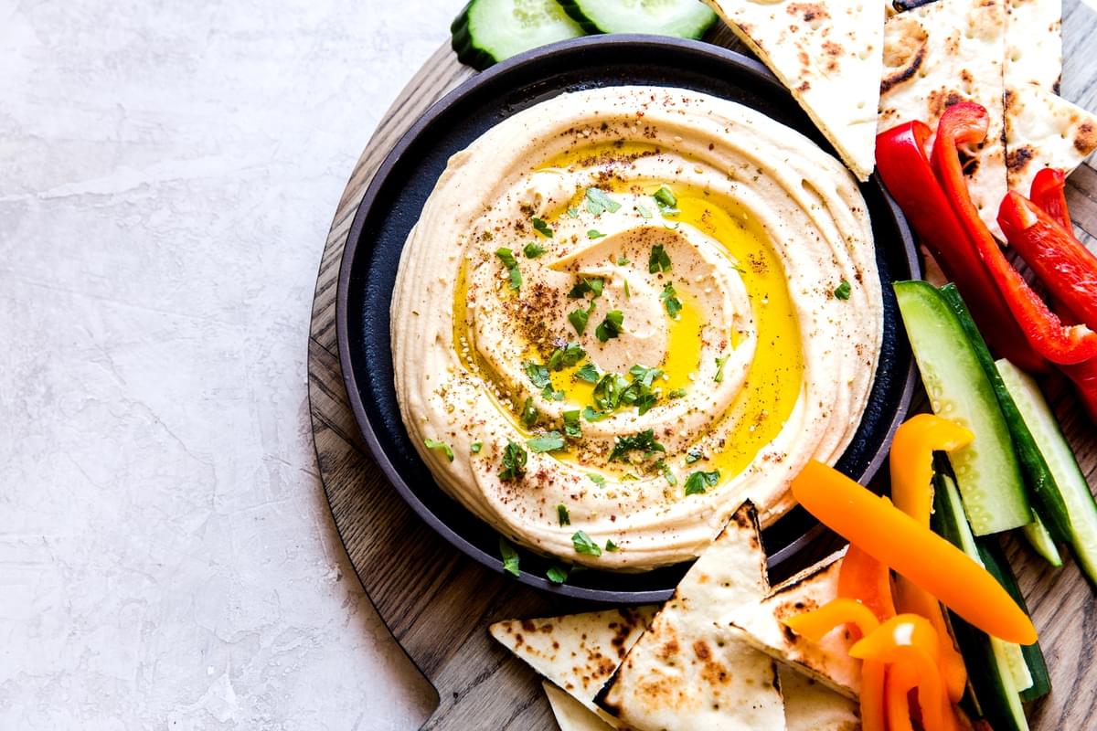 A bowl of homemade hummus on a serving tray with vegetables and pita bread