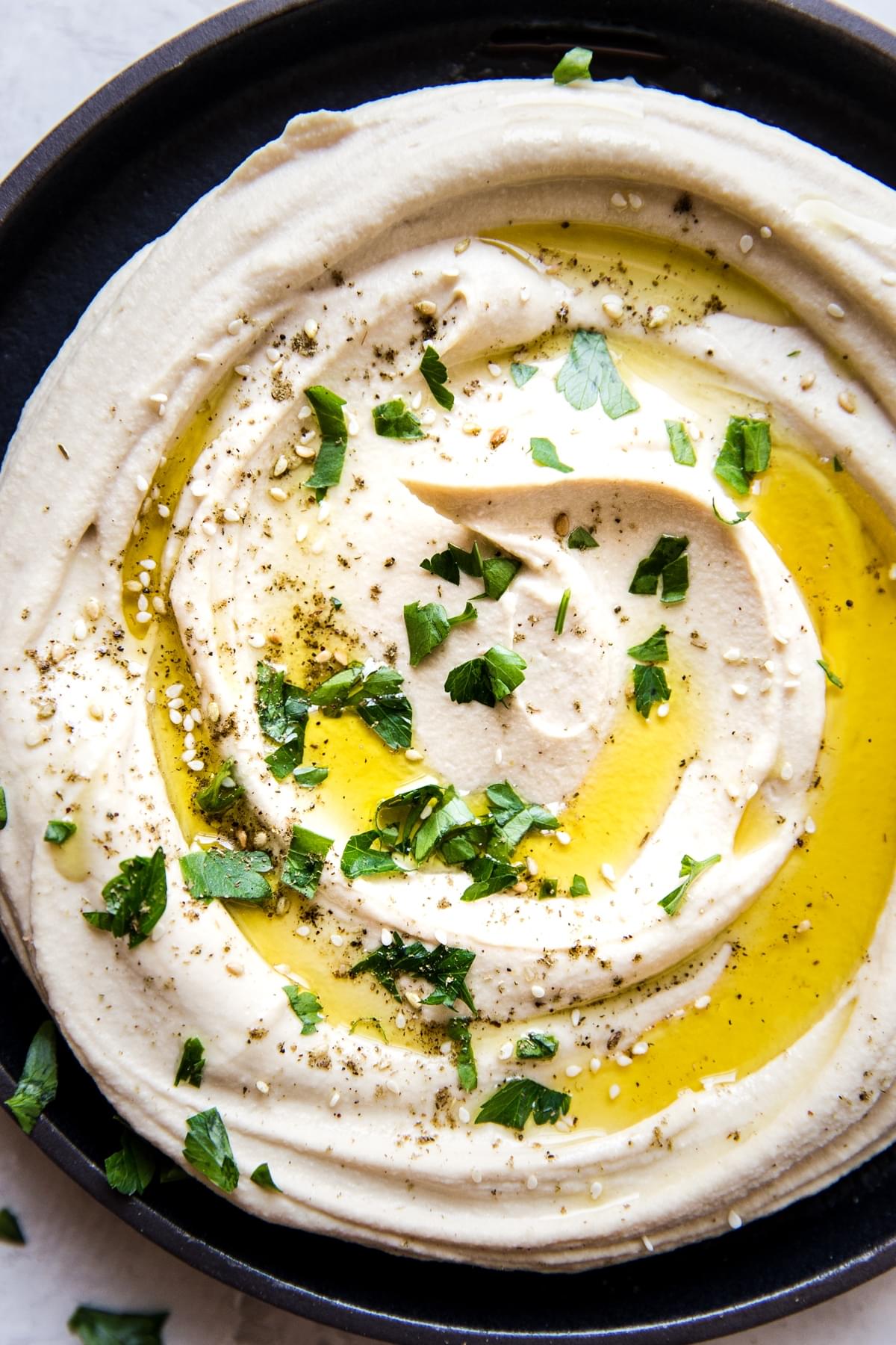 Close up of Creamy homemade Hummus recipe in a bowl with olive oil and parsley