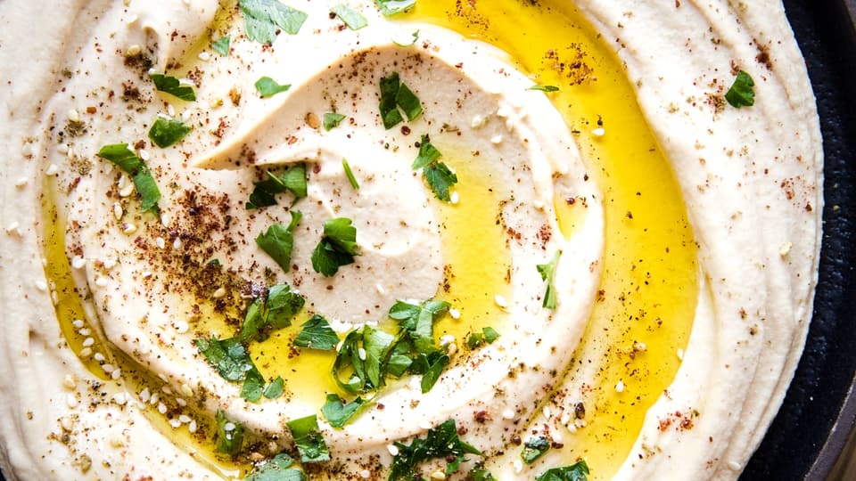 Classic Creamy Hummus with olive oil and parsley in a bowl with pita wedges.