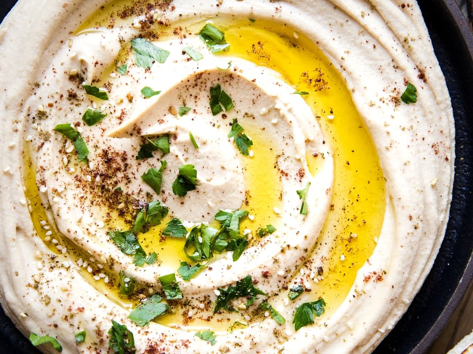 Classic Creamy Hummus with olive oil and parsley in a bowl with pita wedges.