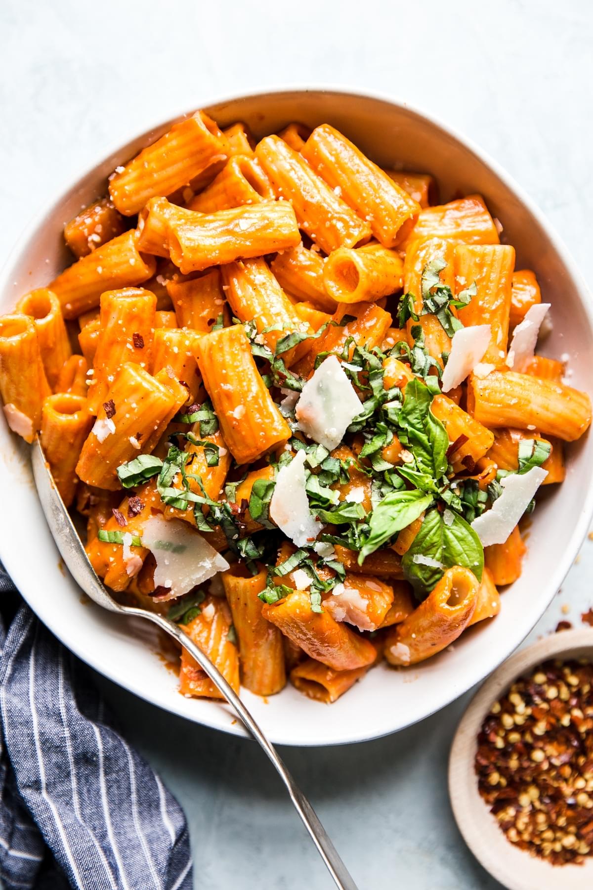 white bowl filled with creamy roasted red pepper rigatoni pasta topped with fresh parmesan, fresh basil and red pepper flakes