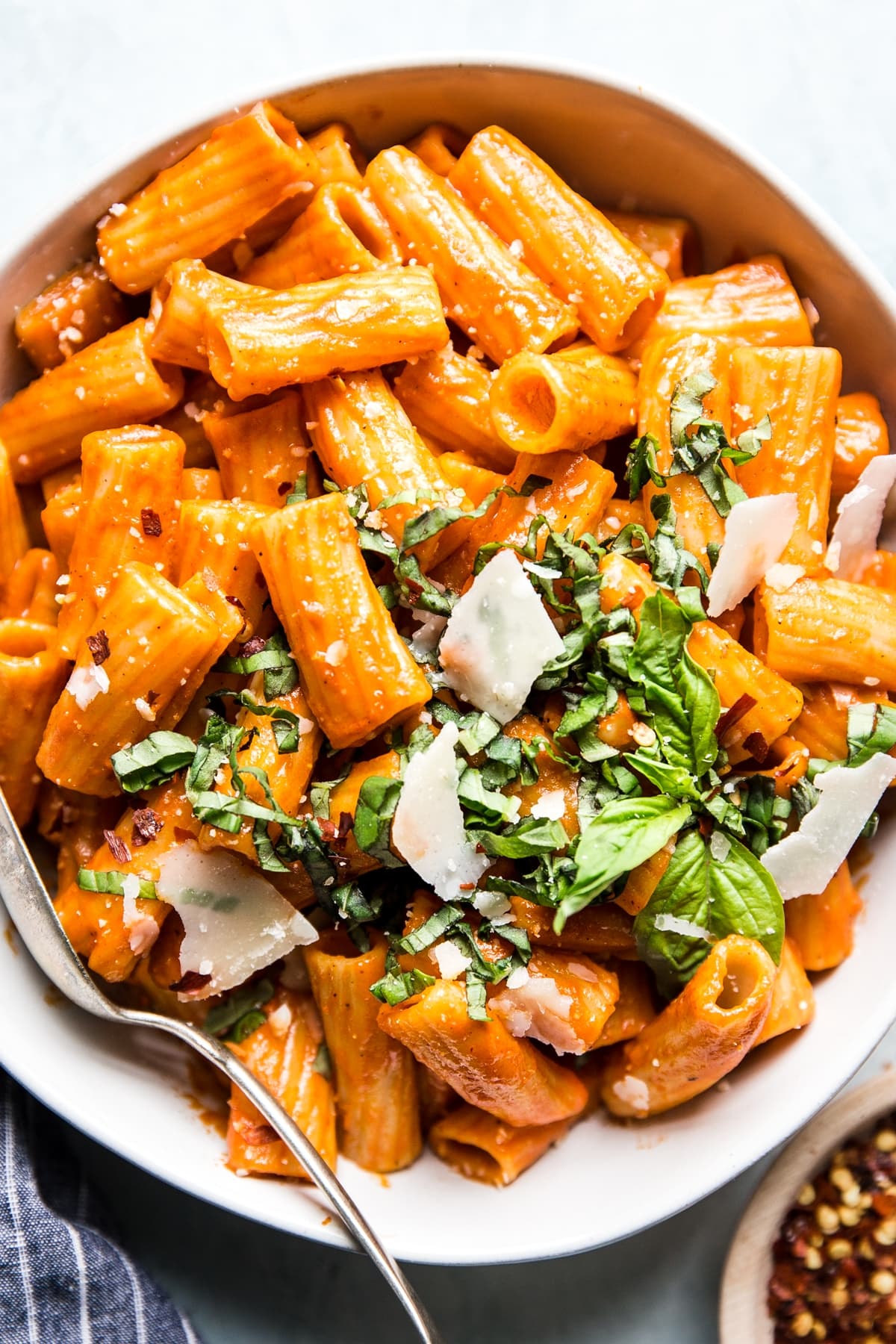 bowl of creamy roasted red pepper rigatoni pasta topped with fresh parmesan cheese and basil