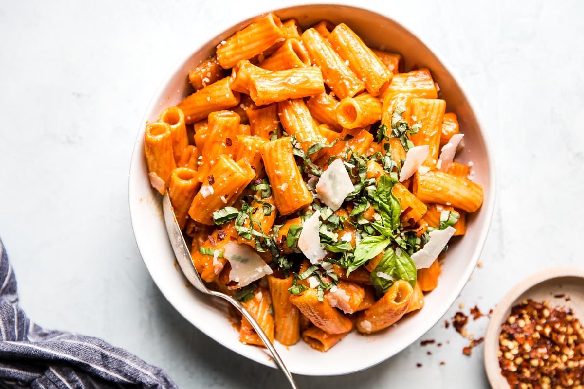 large bowl filled with creamy roasted red pepper rigatoni pasta topped with fresh parmesan and fresh basil