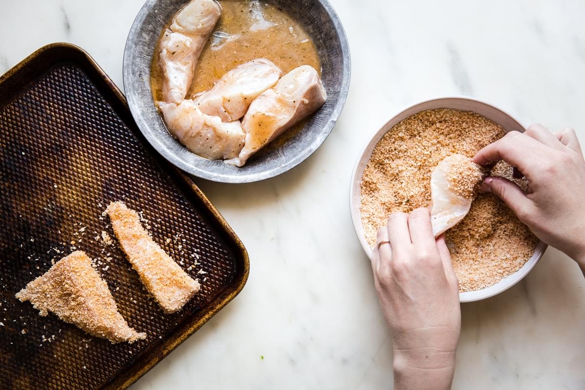 hands dipping marinated white fish into panko