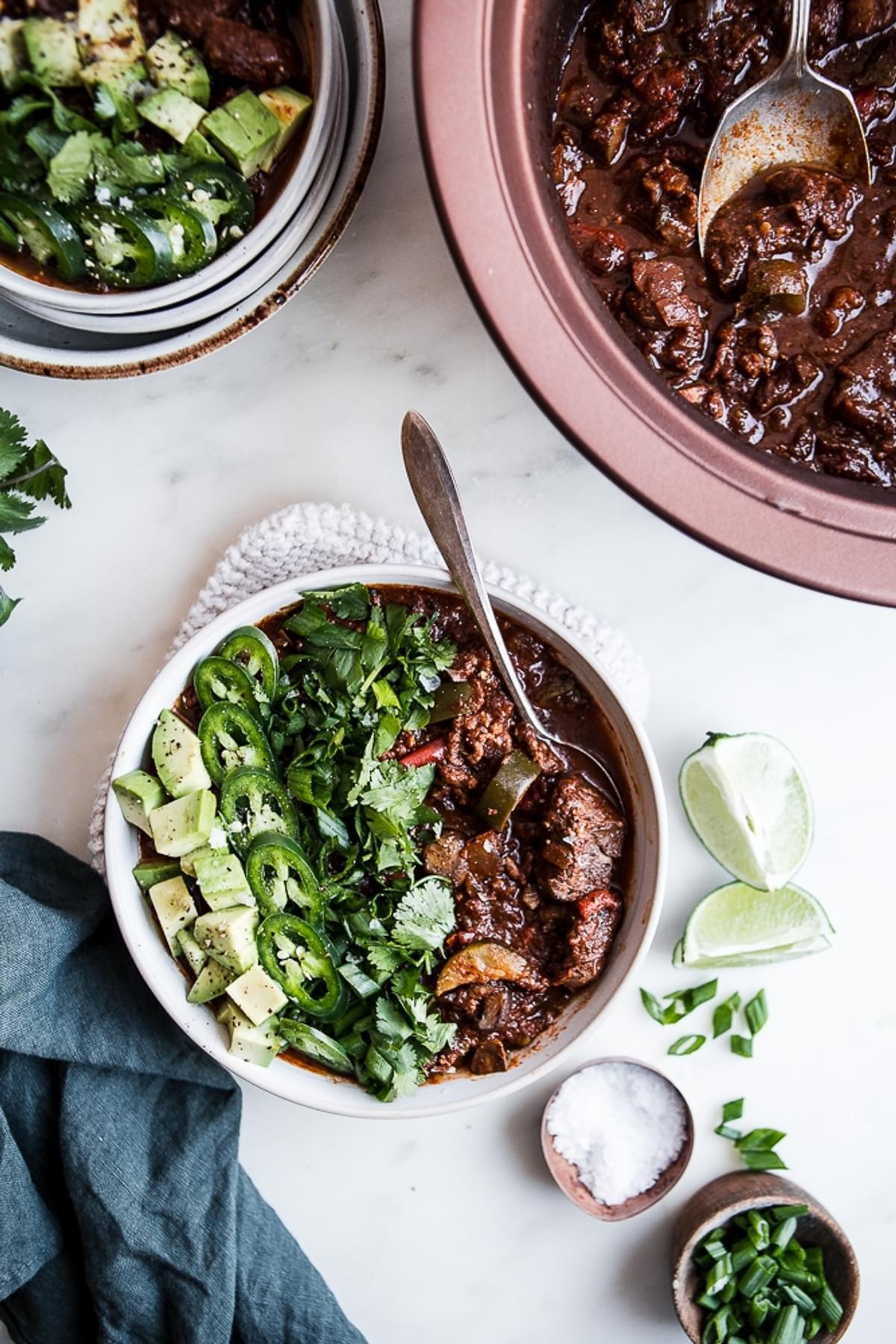 low carb crock pot paleo chili served in bowls and topped with fresh cilantro, jalapenos and sliced avocados