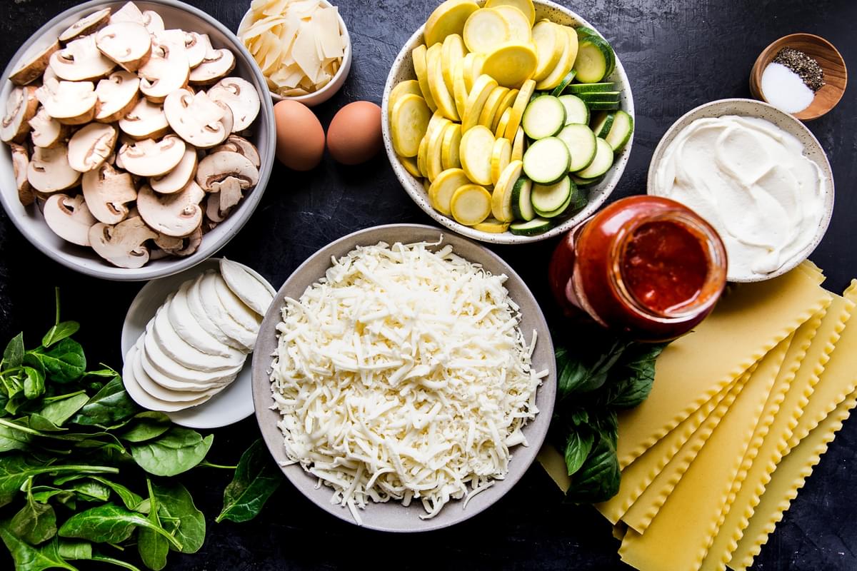 ingredients laid out for vegetarian lasagna mushrooms, eggs, parmesan cheese, mozzarella cheese, pasta, ricotta, zucchini