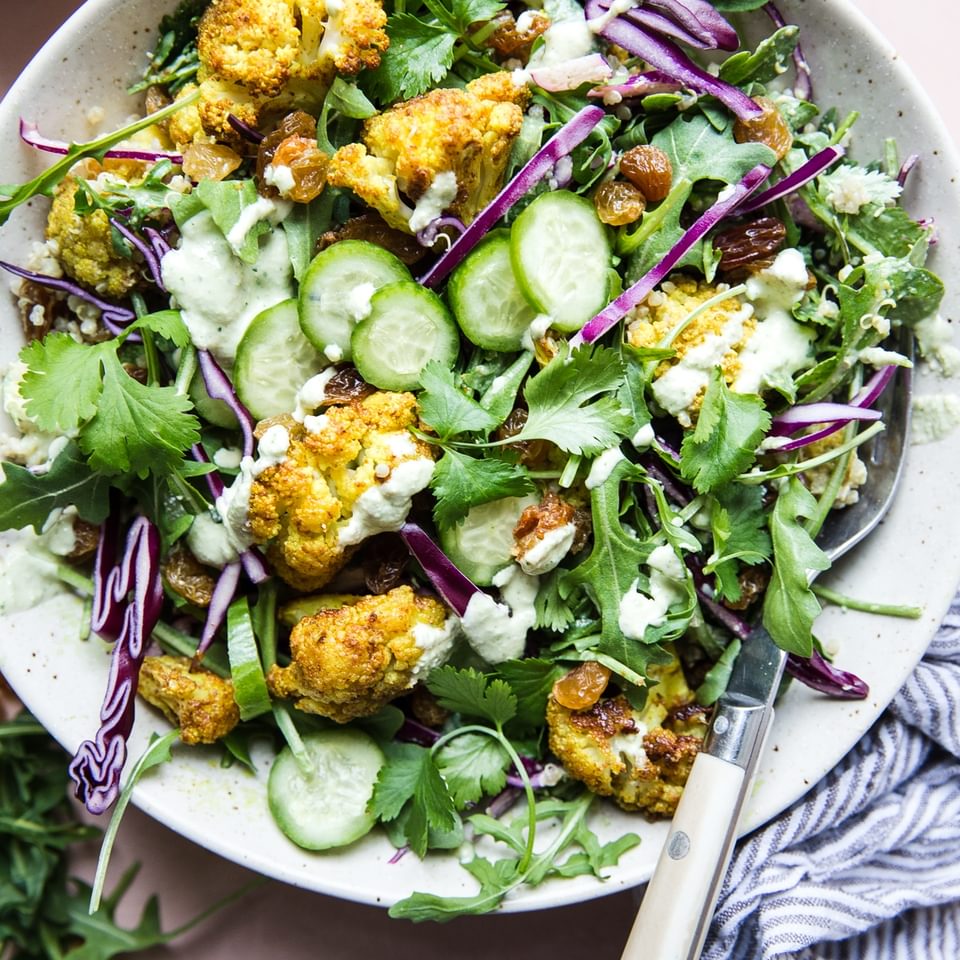 Curried Cauliflower Quinoa Salad with tahini dressing with cucumber and cabbage in a bowl with a fork