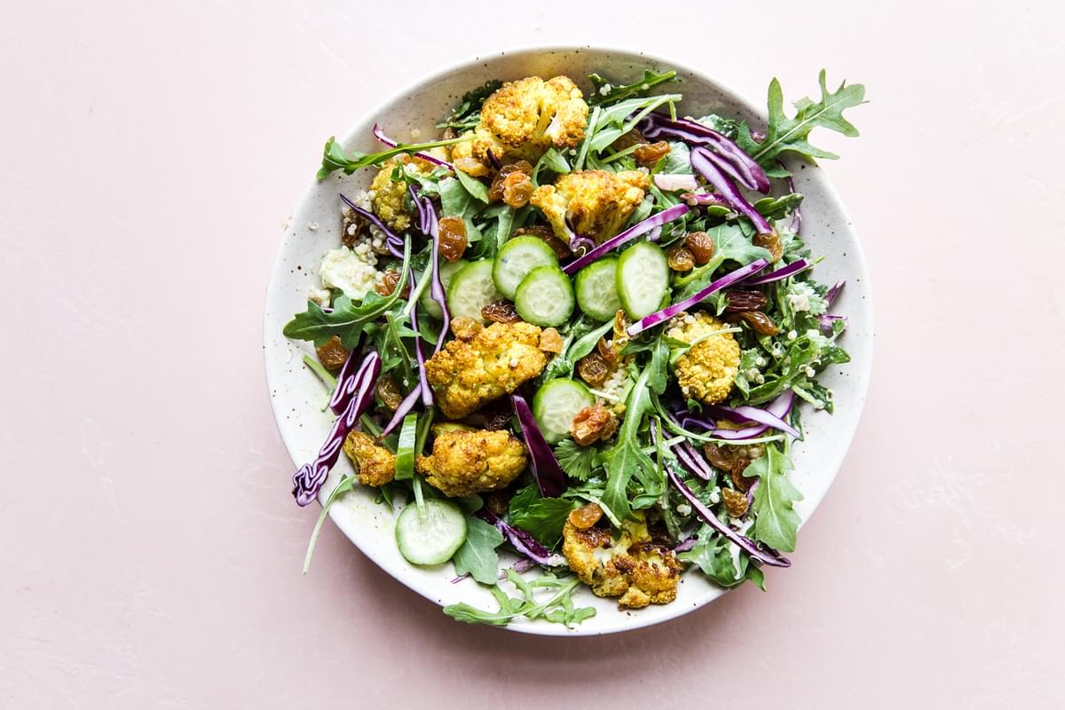 Curried Cauliflower Quinoa Salad with tahini dressing with cucumber and cabbage in a bowl