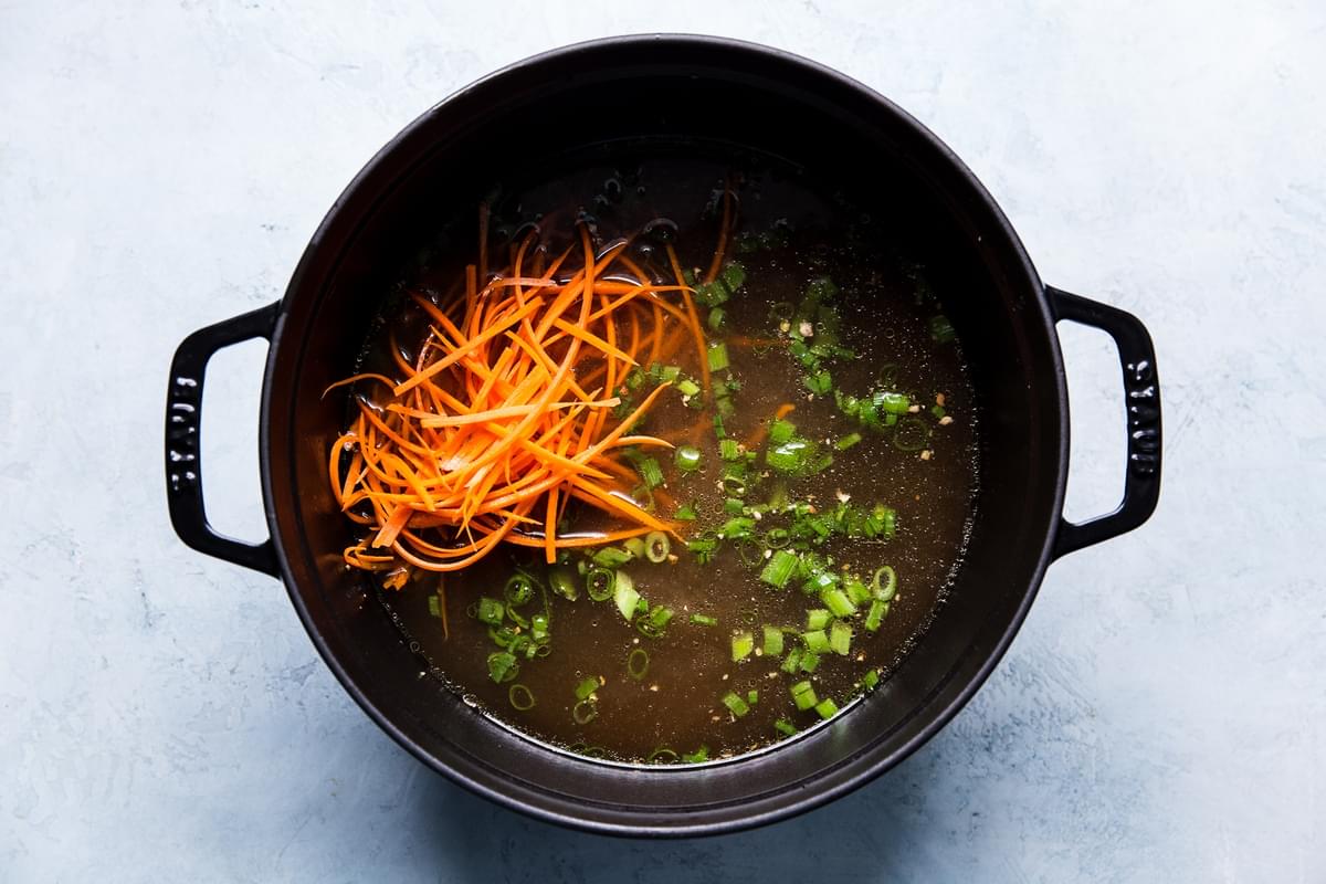 julienned carrots, green onions, garlic and ginger in a pot with broth