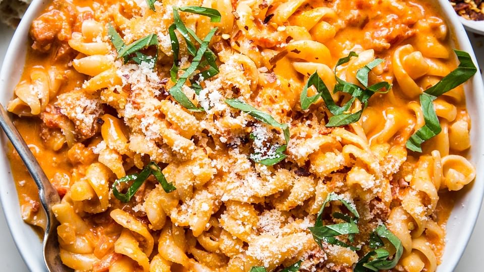a bowl of pasta tossed with easy vodka sauce sprinkled with red pepper flakes, parmesan cheese and basil.