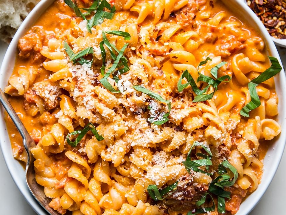 a bowl of pasta tossed with easy vodka sauce sprinkled with red pepper flakes, parmesan cheese and basil.