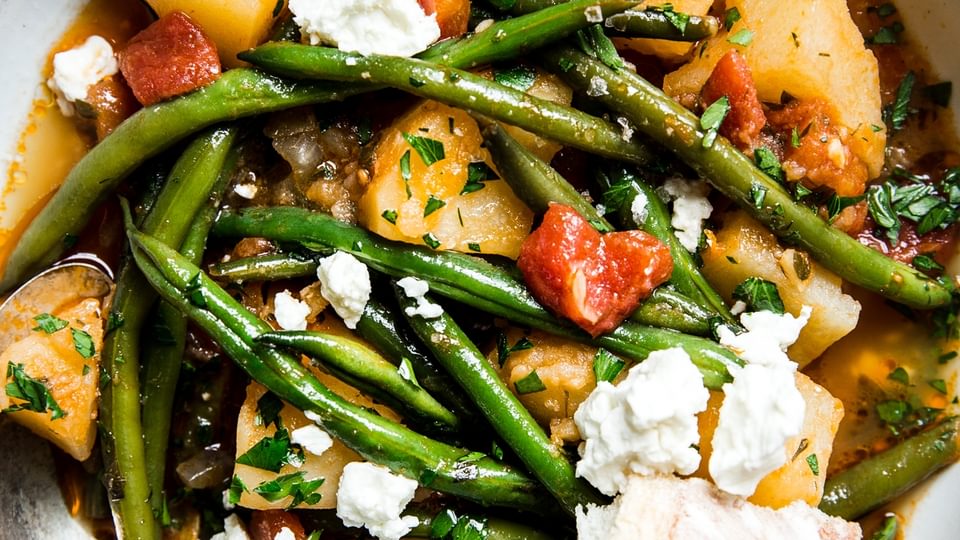 A bowl of fasolakia Greek green beans with feta and crusty bread