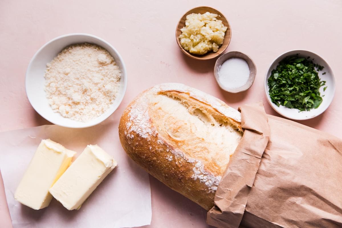 Ingredients for perfect garlic bread; crusty bread, fresh parsley, parmesan cheese, garlic, butter and salt