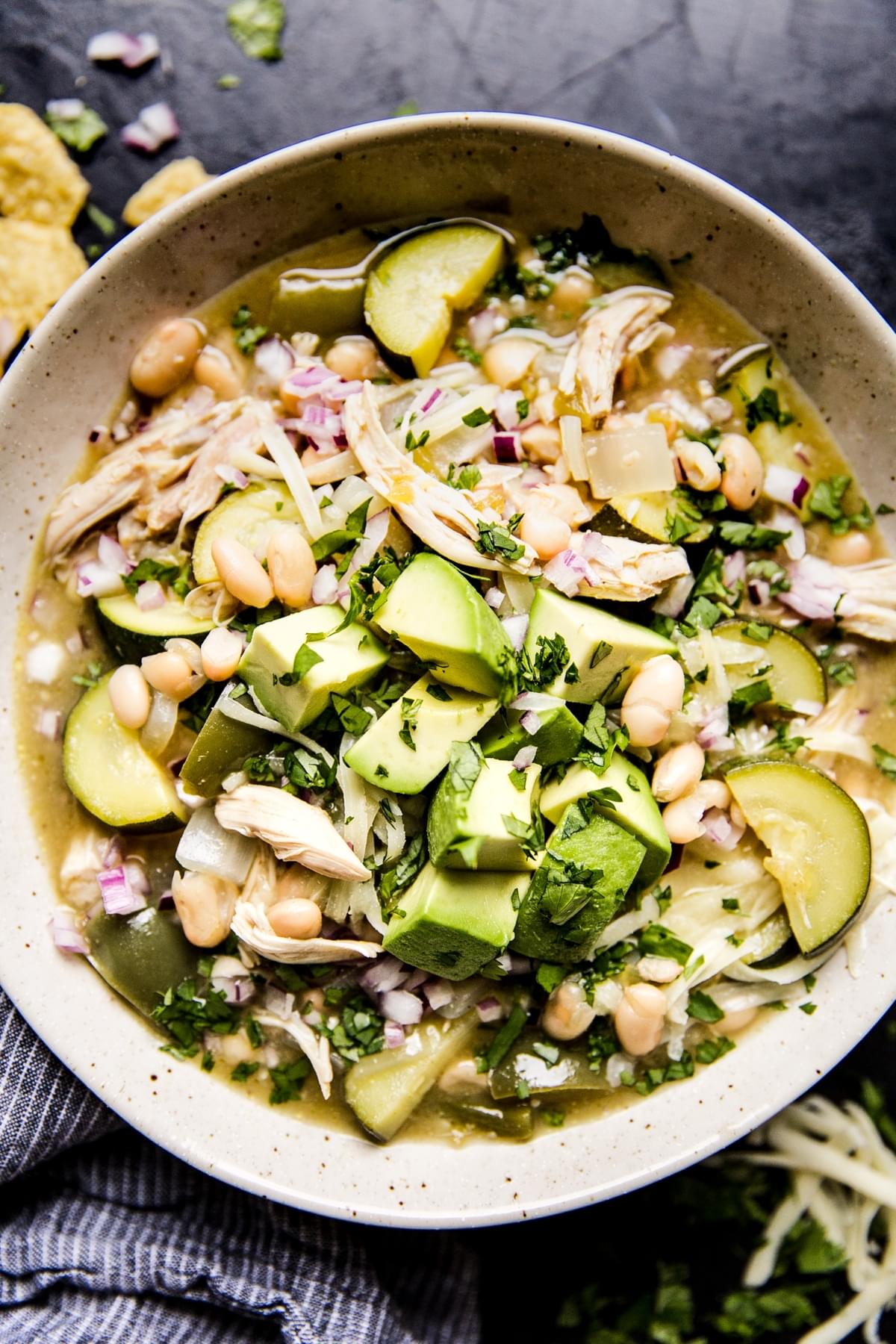Green Chicken Enchilada Soup in a bowl with avocado and zucchini