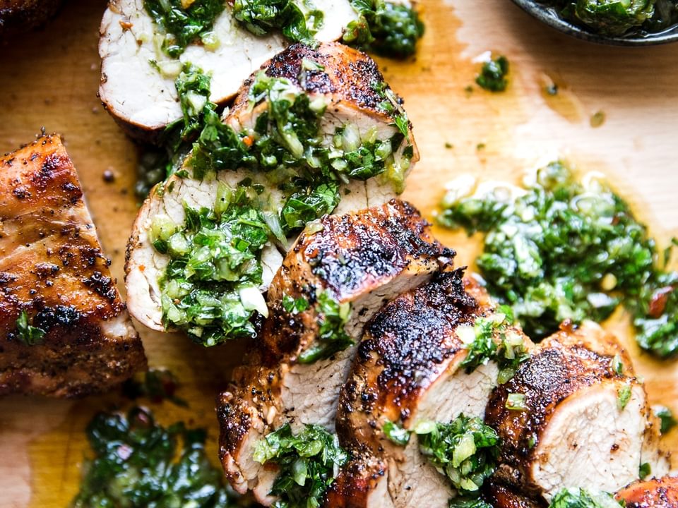 Grilled Pork Tenderloin sliced on a cutting board With Chimichurri