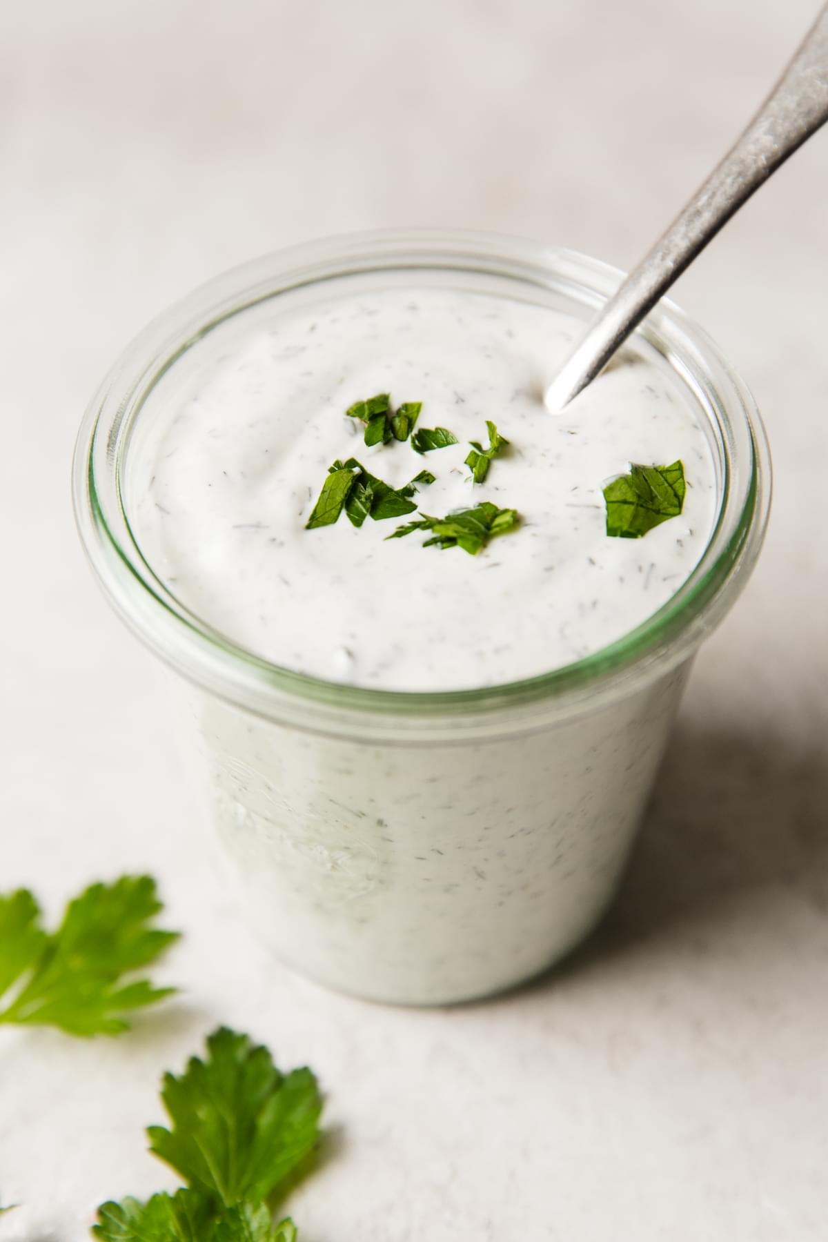 a glass jar filled with homemade ranch dressing topped with fresh parsley