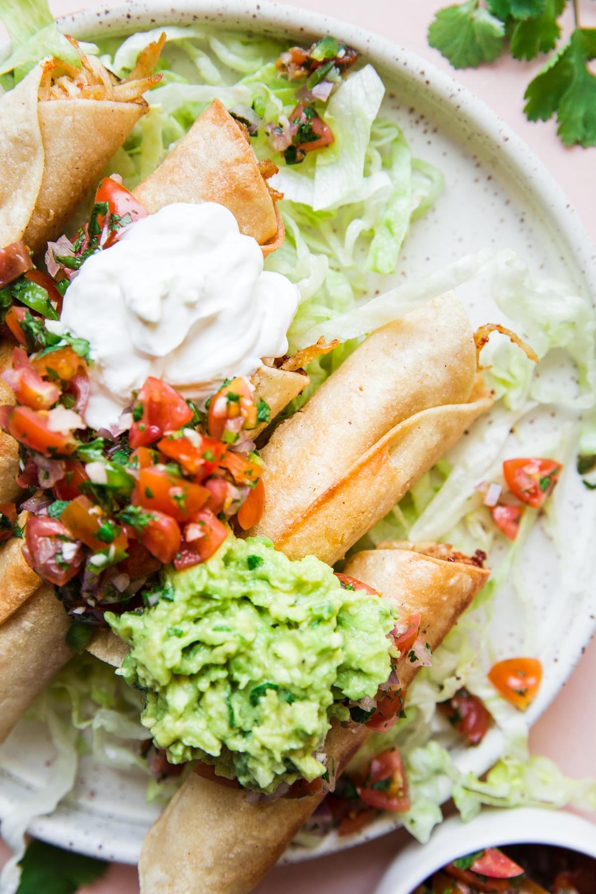 Homemade Chicken Taquitos on a plate with guacamole, sour cream, salsa and lettuce