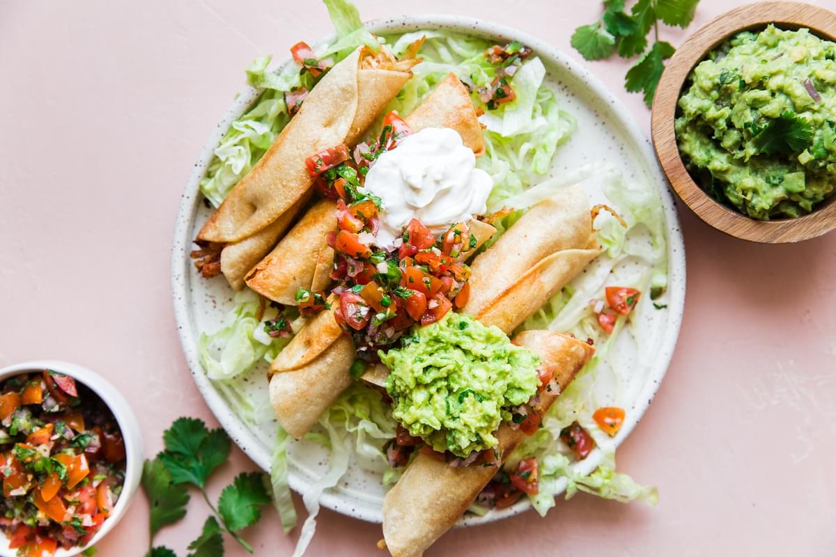 Homemade Chicken Taquitos on a plate with guacamole, sour cream, salsa and lettuce