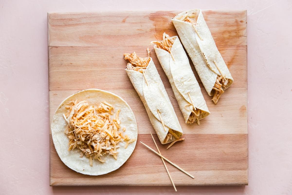 Homemade Chicken Taquitos being assembled with toothpicks on a cutting board